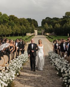 a bride and groom walk down the aisle as guests look on from behind them in tuxedos