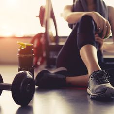 a woman sitting on the floor with her feet up next to a barbell and bottle of water