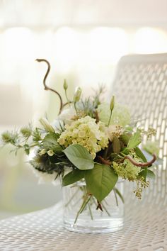 a vase filled with white and green flowers on top of a wooden table next to a chair