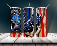 three patriotic cups with straws in them on a wooden table, one has an american flag and the other is a blue cross