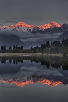 the mountains are covered in clouds and reflecting in the still water at sunset or dawn