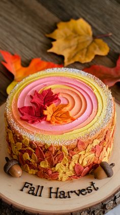 a colorful cake with frosting and leaves on the top is sitting on a wooden plate