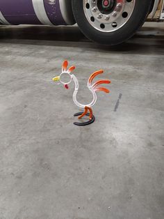 an orange and white rooster figurine sitting on the ground next to a bus