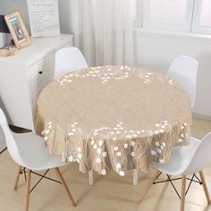 a round table with white chairs and a beige tablecloth on it in front of a window