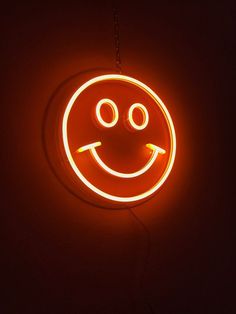 a smiley face neon sign hanging from the side of a wall in a dark room