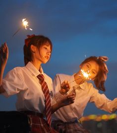 two girls in school uniforms are holding sparklers