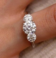 a woman's hand holding a three stone diamond ring