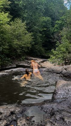 two people are in the water near some rocks and trees, while one person is swimming