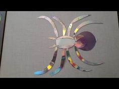 a spider made out of colored paper on top of a white sheet of paper with scissors next to it