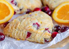 cranberry orange scones with icing sitting on wax paper next to sliced oranges