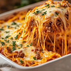 a close up of spaghetti being lifted from a casserole dish with meat and cheese