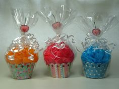 three colorful cupcakes wrapped in clear cellophane and tied with ribbons on white background