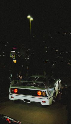 the back end of a white car parked in front of a parking lot at night