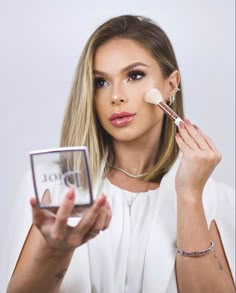 a woman is holding a compact brush and looking at the camera