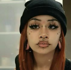 a woman with red hair and piercings on her nose wearing a beanie hat