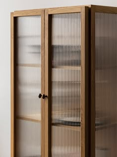 a tall wooden cabinet with glass doors on the front and bottom sides, sitting against a white wall