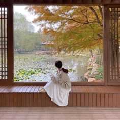 a woman sitting on top of a wooden bench next to a window filled with water