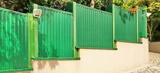 a green fence is next to a white wall