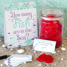 a jar filled with red candy next to a sign and some sea shells on the ground