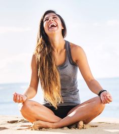 a woman sitting in the sand with her eyes wide open and smiling at the camera