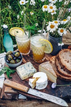 cheese, bread and olives are on a cutting board with flowers in the background