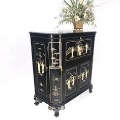 a black and gold painted cabinet with flowers on top