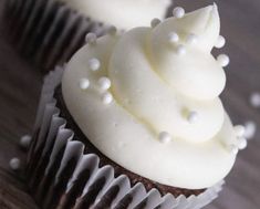 two cupcakes with white frosting and sprinkles sitting on a table