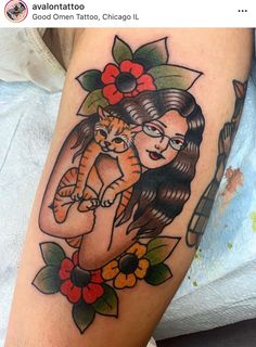 a woman holding a cat on her arm with flowers and leaves around her neck,