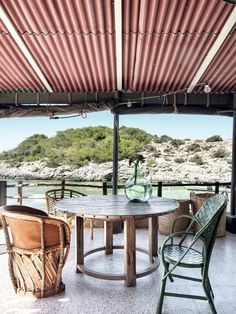 an outdoor table and chairs under a covered area with water in the backgroud