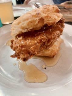 a fried chicken sandwich is sitting on a white plate with sauce drizzled around it