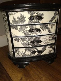 an ornate black and white dresser with trees on it's drawers, sitting on a wooden floor