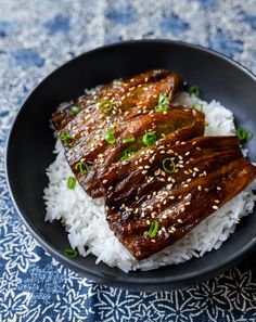 a black plate topped with rice and meat on top of a blue table cloth covered in green onions