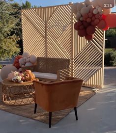 a chair and table with balloons hanging from it's sides on the ground in front of a wall