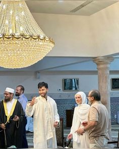 a group of people standing around each other in a room with chandelier hanging from the ceiling