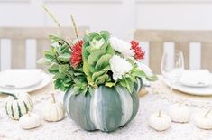 a table with white and red flowers in a green pumpkin shaped vase on top of it