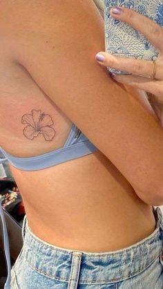 a woman with a small flower tattoo on her left side ribcage is holding a cell phone in her right hand