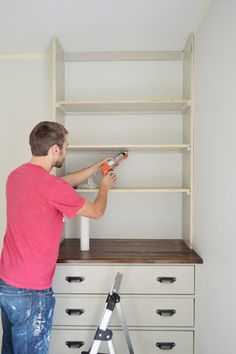 a man is using a paint roller to paint the bottom of a bookcase in his bedroom