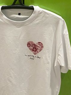 a white t - shirt with a red heart printed on the chest and words written across the chest