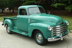 an old green truck is parked on the street