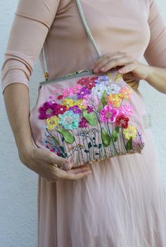 a woman in a pink dress is holding a purse with flowers on the front and side