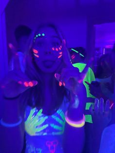 a woman with glow paint on her face and hands in front of the camera at a party