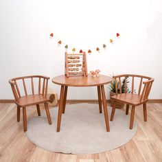 two wooden chairs sitting at a small round table in front of a white wall with autumn decorations on it