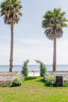 an outdoor ceremony setup with white chairs and palm trees on the beach in front of the ocean