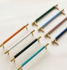 four different colored handles on each side of a white surface with gold tips and two black ends