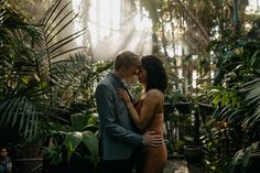 a man and woman standing next to each other in front of some tropical plants with sunlight streaming through the windows