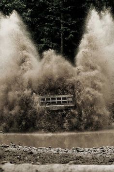 a black and white photo of water splashing over a wooden bench in front of trees