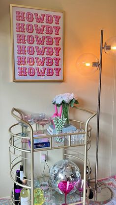 a bar cart with bottles and glasses on it in front of a framed art piece