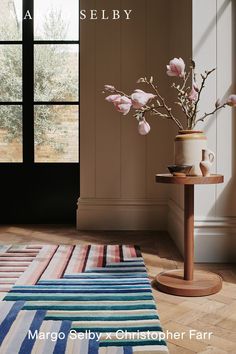 a vase with flowers sitting on top of a wooden table next to a striped rug