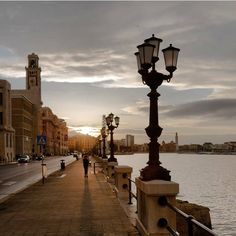 a person walking down a sidewalk next to a body of water with street lamps on either side