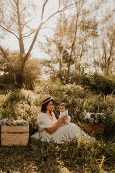 a woman sitting in the grass holding a baby